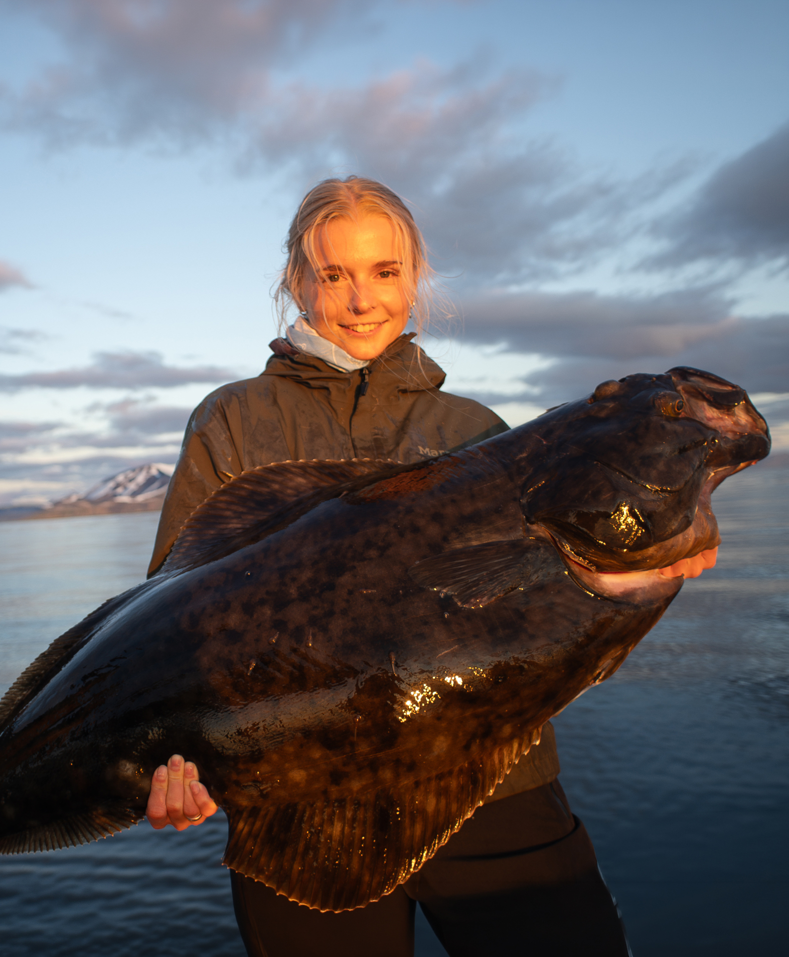 Guest holding a large halibut at dusk on the fjord