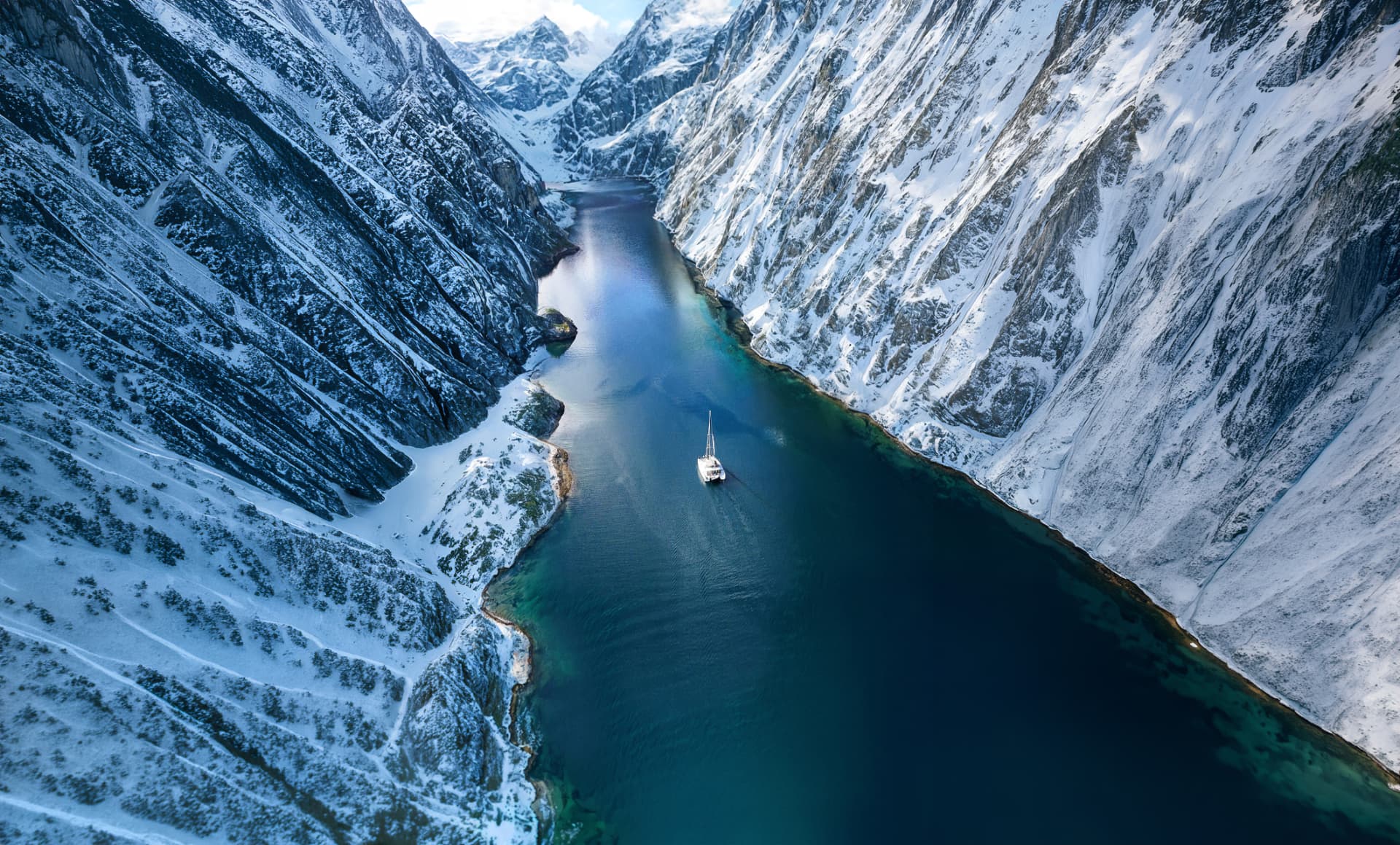 Aerial view of the catamaran sailing through a snowy Arctic fjord