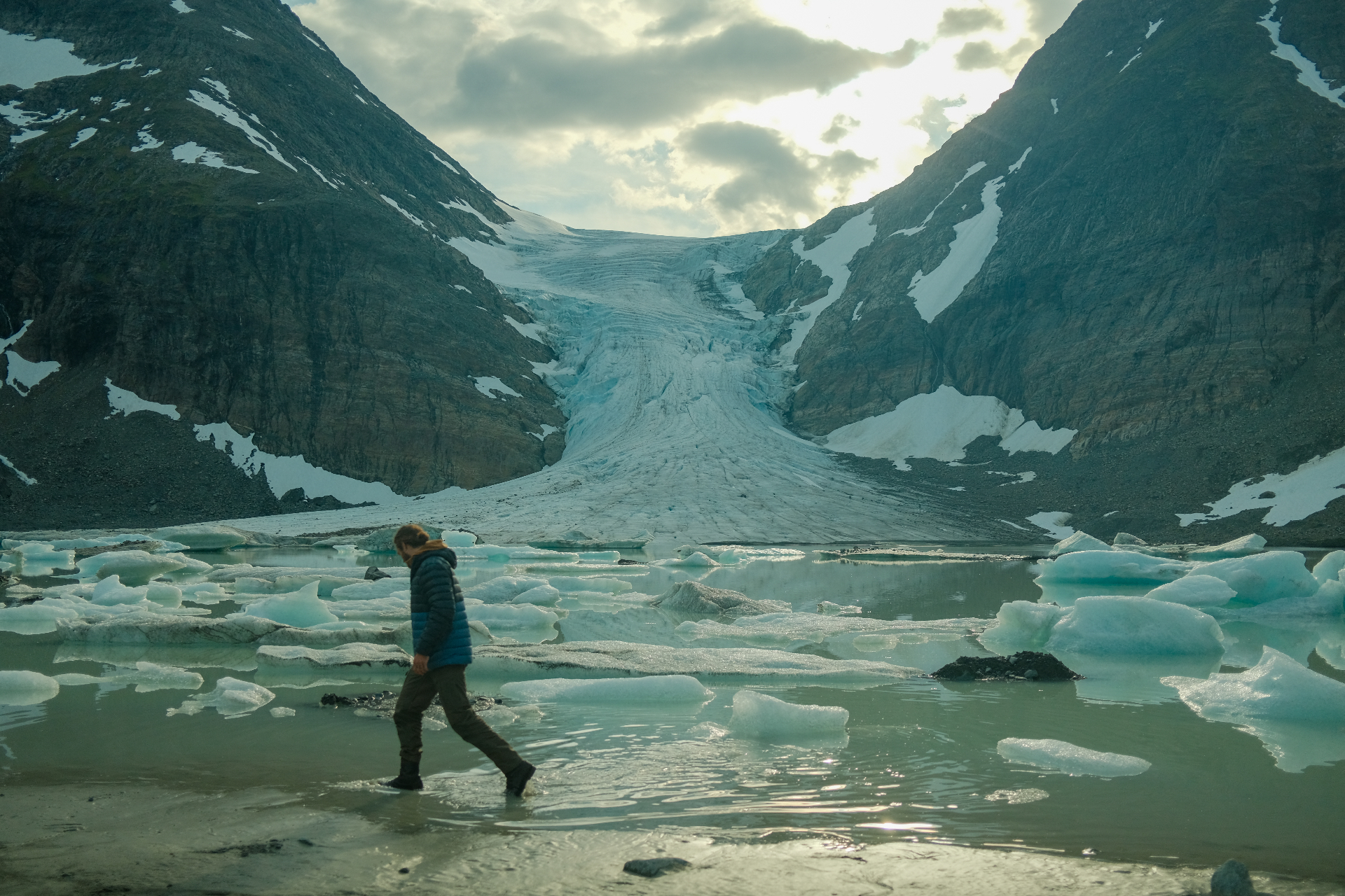Guest walking across a glacial meltwater lagoon beneath Steindalsbreen