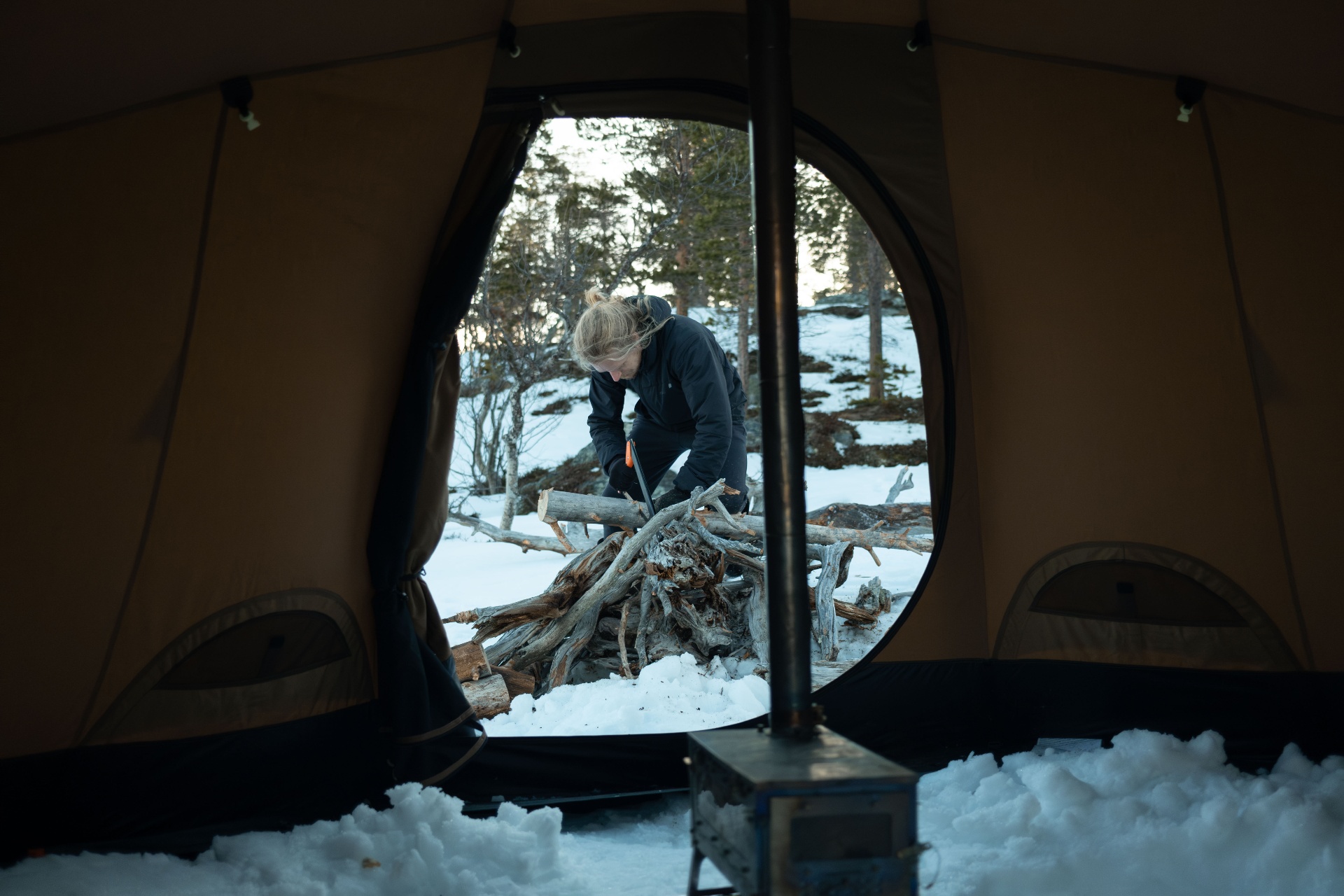 Person preparing firewood outside an Arctic tent