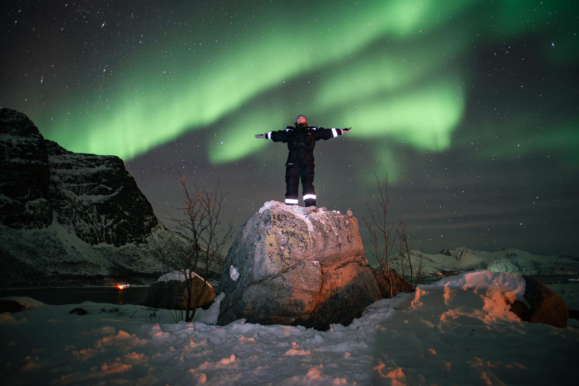 A guest standing on a snow-covered boulder beneath the northern lights