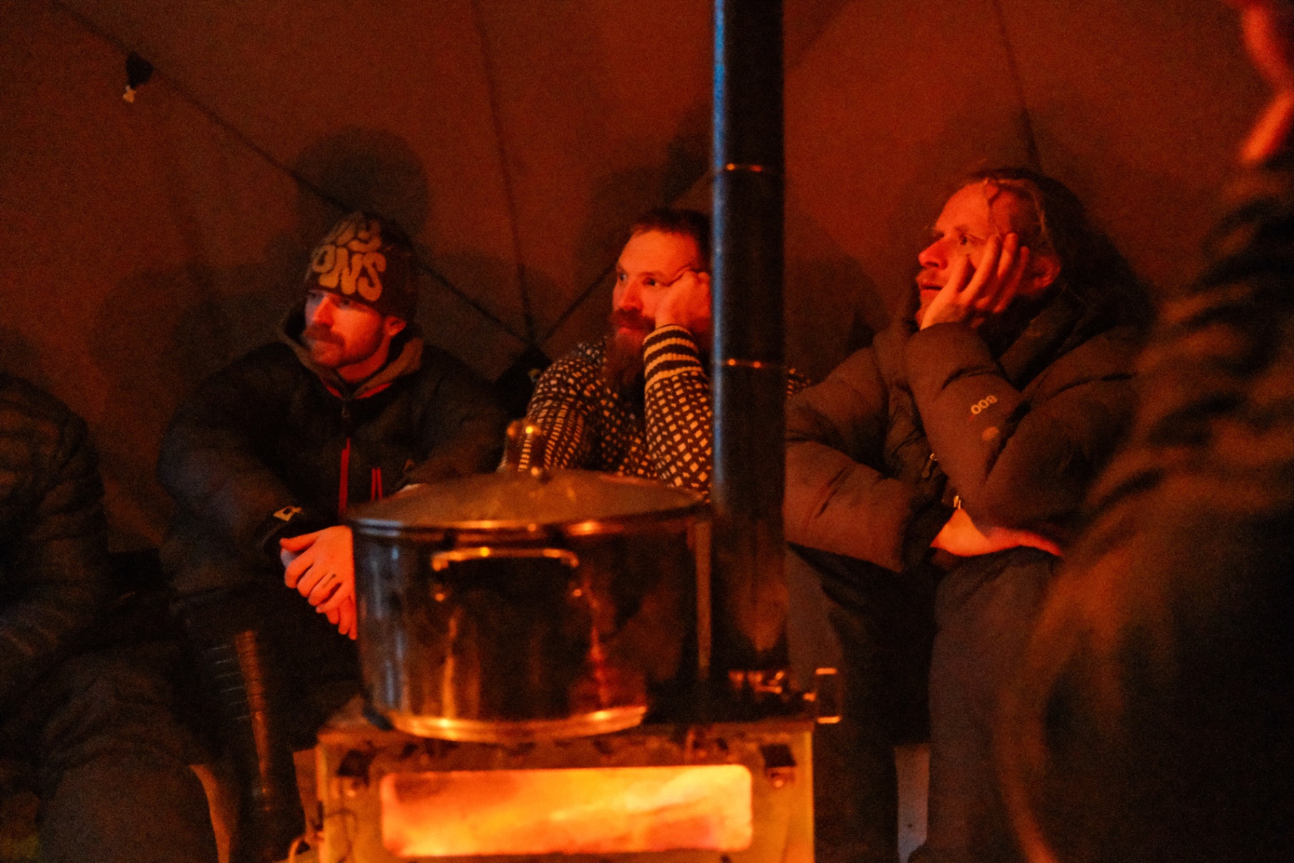 Guests gathered around a wood stove in a warm tent at night