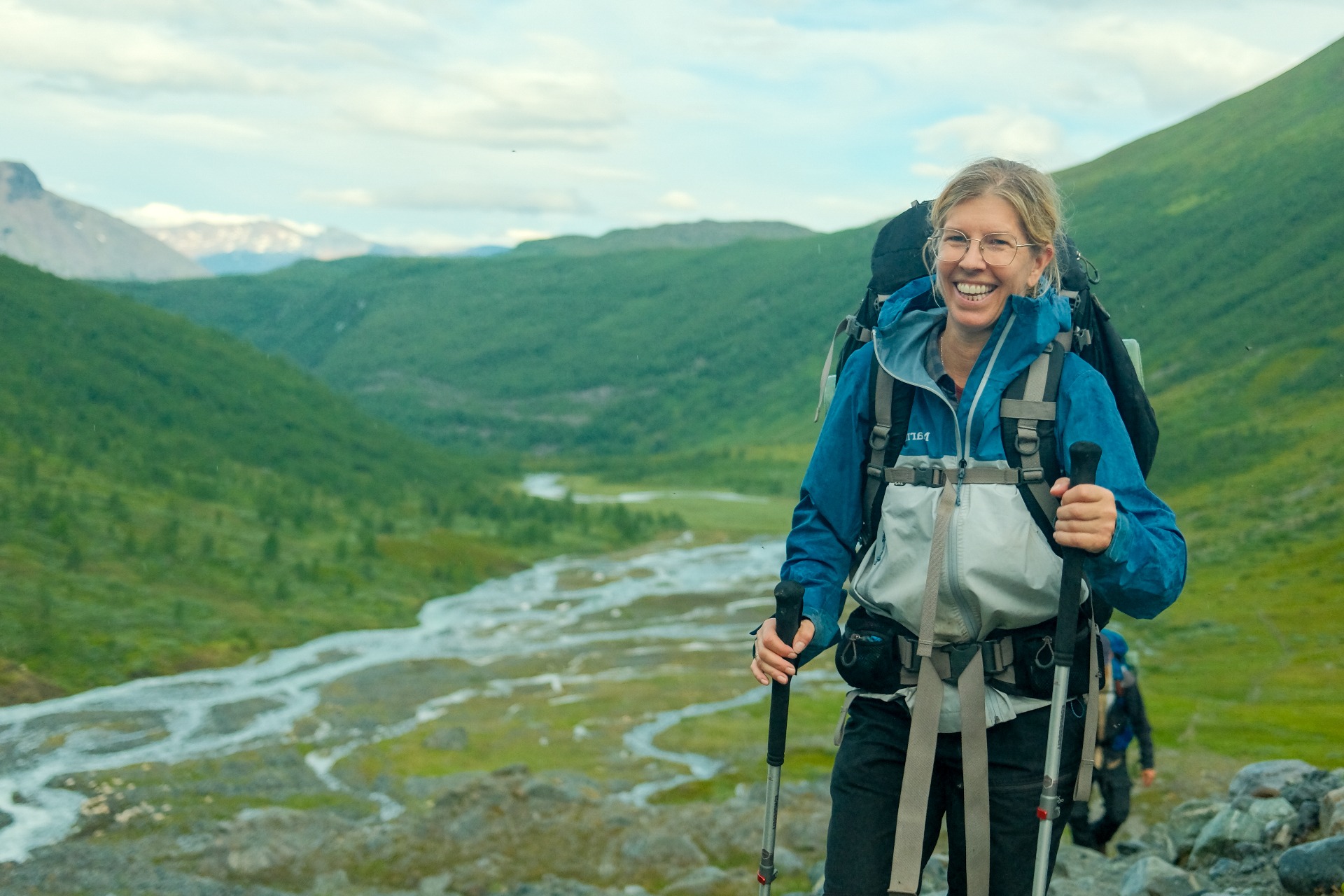 Hiker above a braided river delta in a green Arctic valley