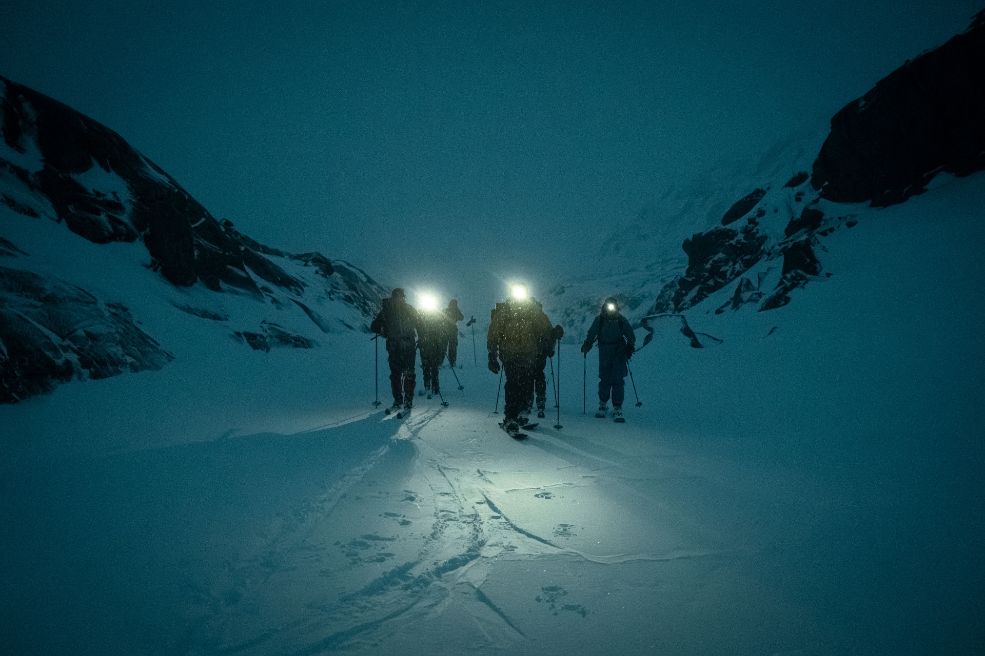 Ski-tourers ascending a snowy couloir under headlamps at dusk