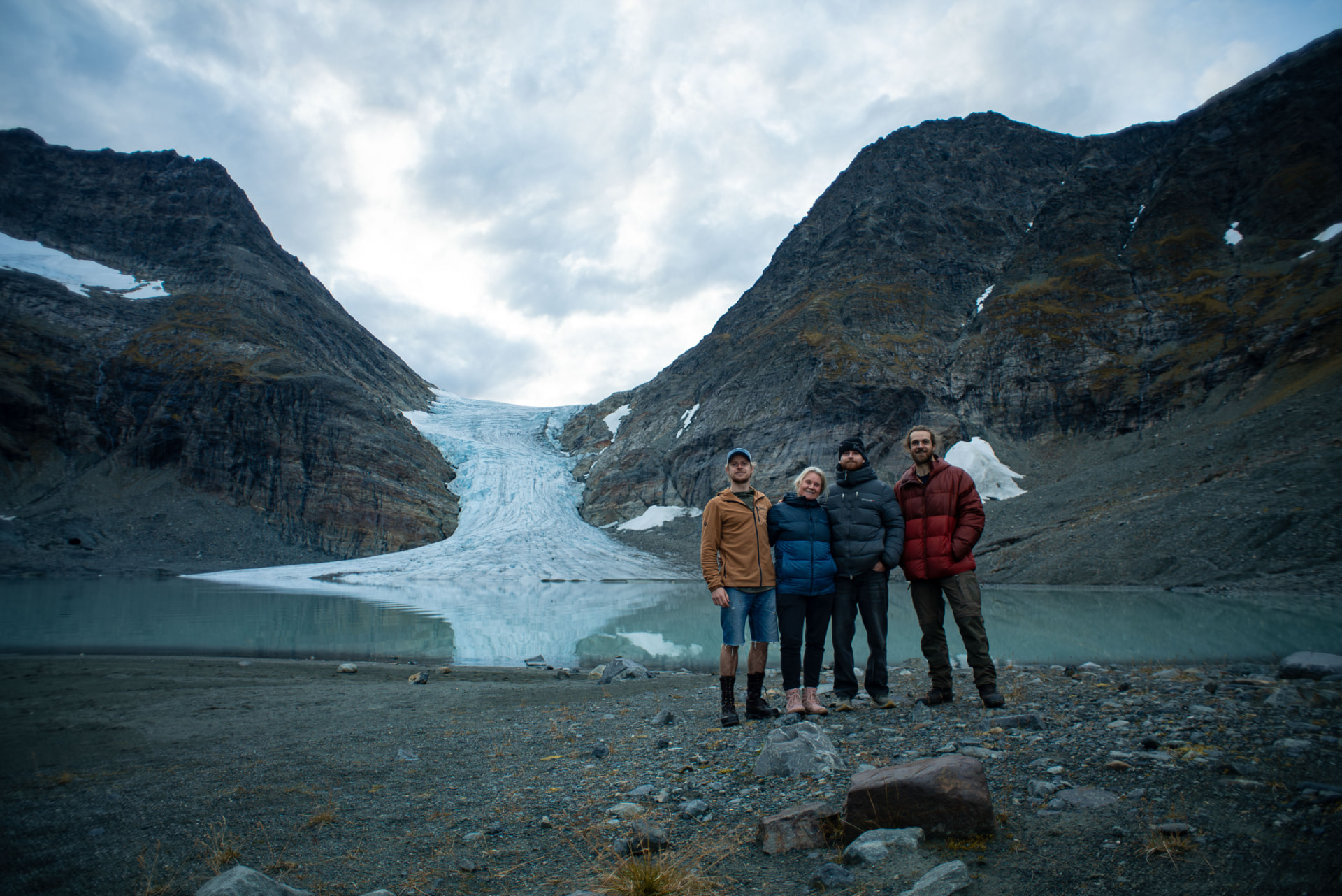 Guests standing at the shore beneath a glacier tongue and its turquoise meltwater lagoon
